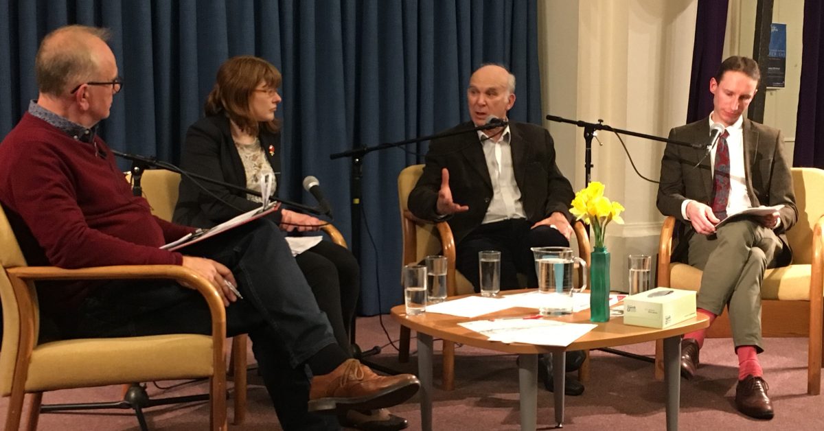 A group of people sit on chairs around a table with microphones in a church building. One of the people is Sir Vince Cable, who was MP for Twickenham at the time.
