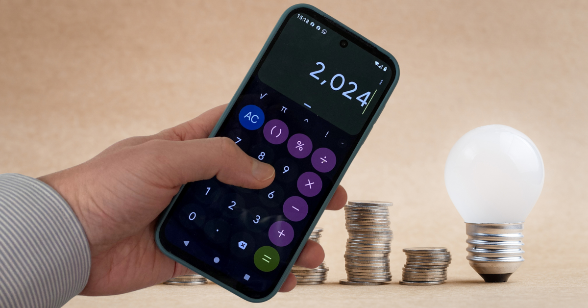 a calculator app is displayed on a mobile phone being held. The background features stacks of coins and a lightbulb