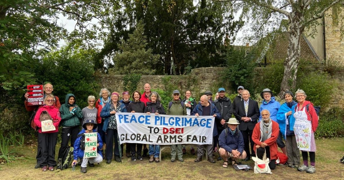 The group of peace pilgrims to the arms fair holding a banner standing in front of some trees