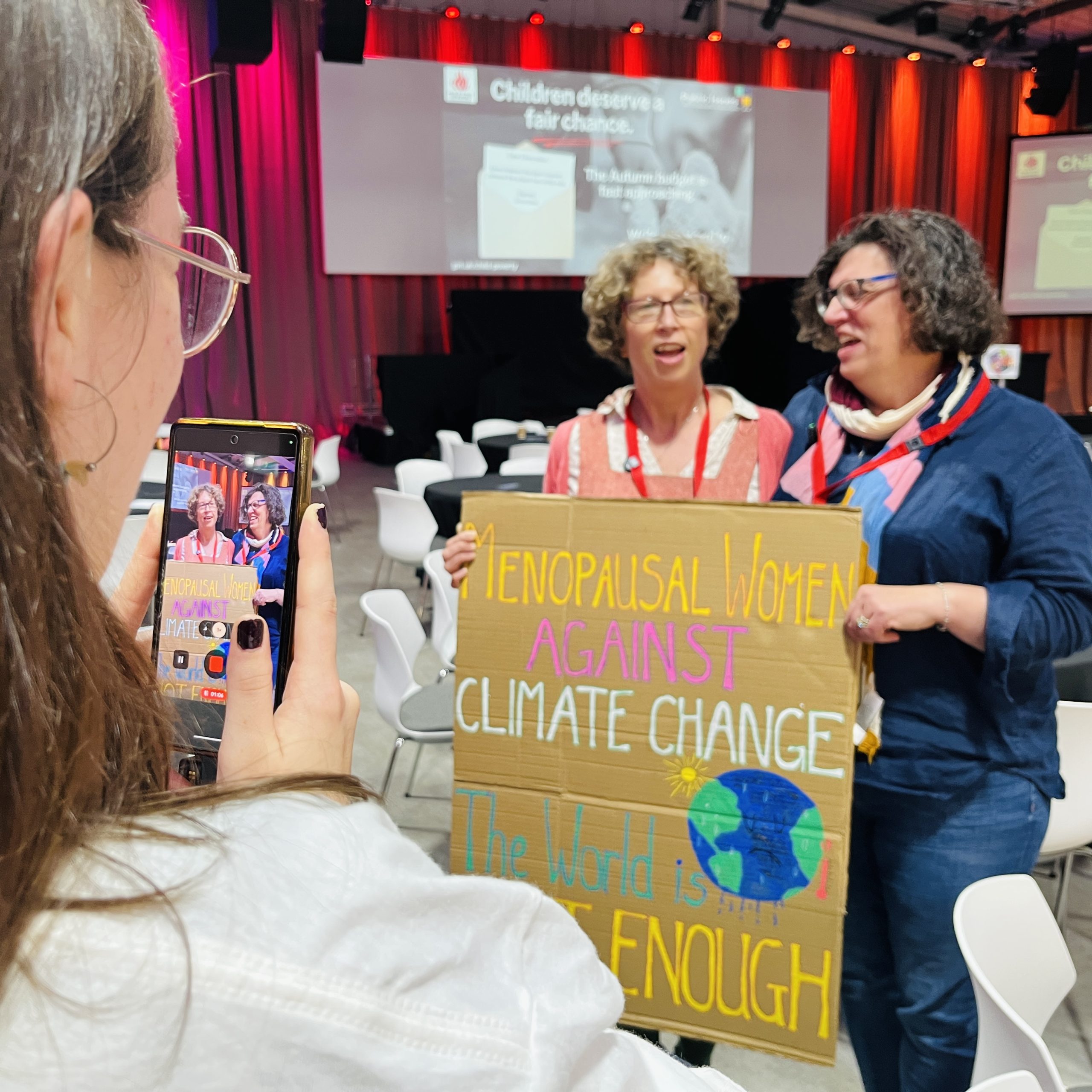 JPIT's Erica Lees-Smith photographing two participants with a protest banner at ForGood25 (Photo by Steve Walker)